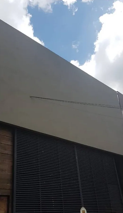 A mesma fachada pronta: a parte de cima fechada e pintada de cinza, lisa, sobre a porta de ripas escuras, com céu azul ao fundo