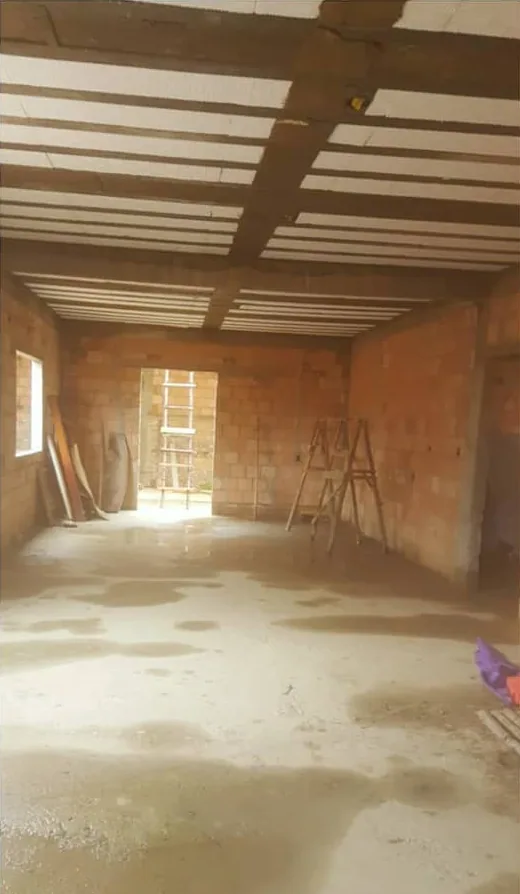Salão em obra antes do gesso: paredes de tijolo à vista, laje de vigotas no teto e piso de cimento molhado
