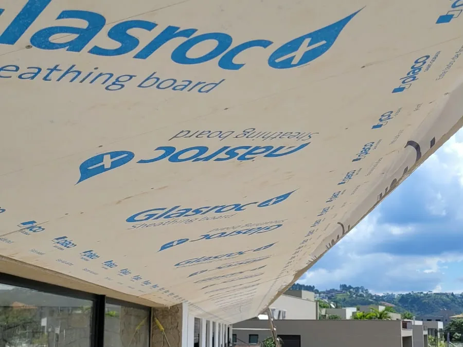 Placa Glasroc X fixada sob o beiral de uma fachada, vista de baixo, sobre as janelas, com o céu e a vizinhança ao fundo