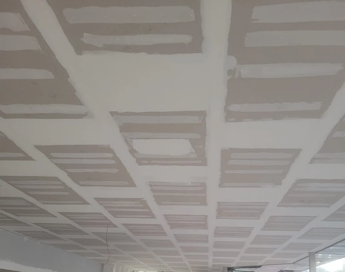 Forro de gesso em quadros num salão comercial: placas separadas por faixas de massa, com as juntas em acabamento, vistas em perspectiva até a fachada de vidro