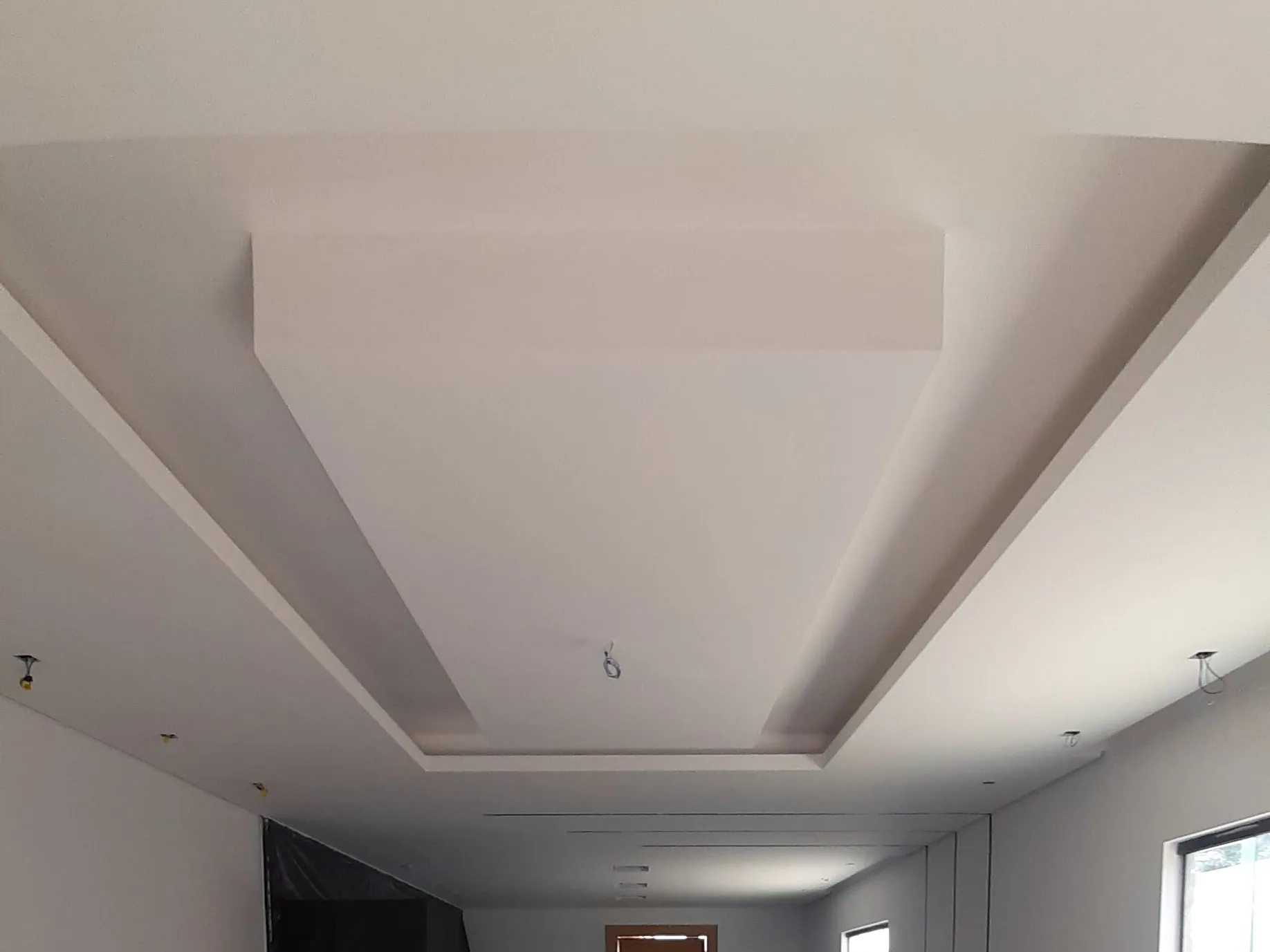 Forro de gesso liso e branco com um rebaixo em degrau no centro, sobre um salão comprido de paredes lisas