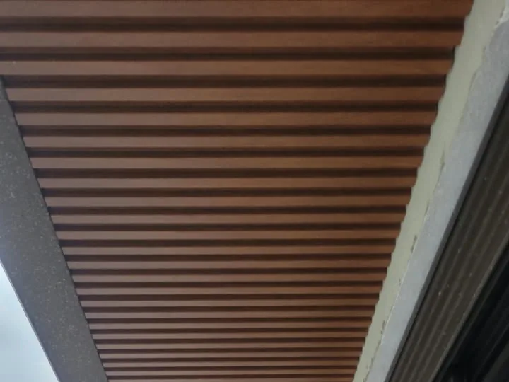 Forro ripado de PVC cor de madeira no beiral de uma casa em obra, com as réguas em perspectiva até a quina de uma viga cinza