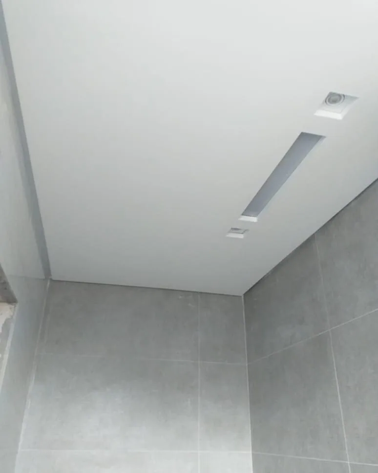 Casa na Península dos Pássaros, em Alphaville: banheiro com revestimento cinza nas paredes e forro de gesso com um recorte linear embutido e um spot