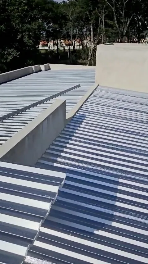Quadro do vídeo: telhado de telha metálica pronto, com platibandas de concreto e árvores ao fundo